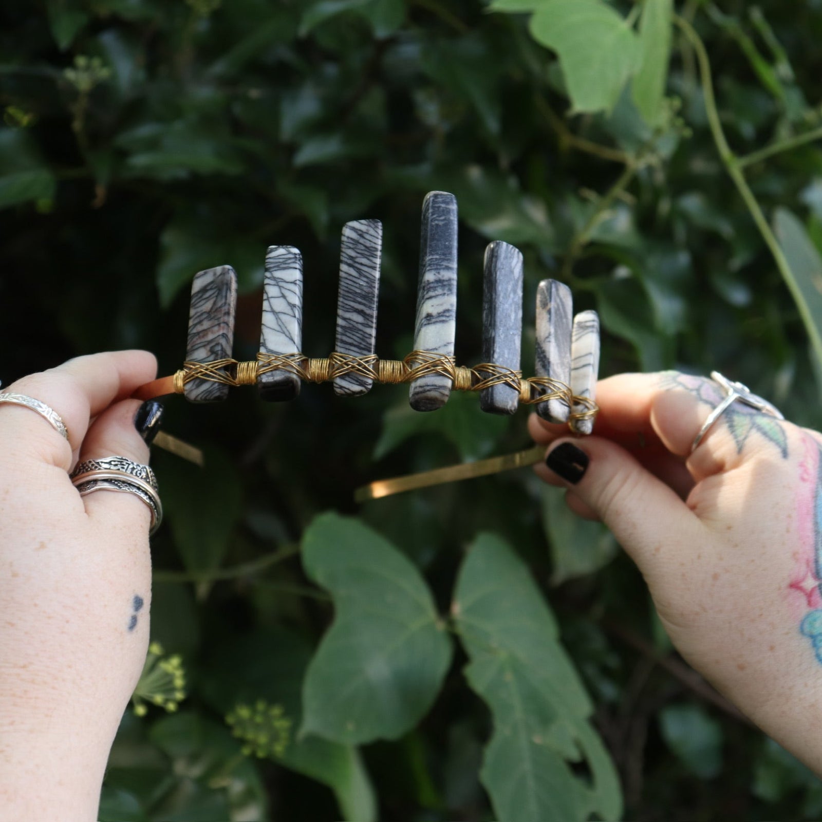 Someone holding the Fairy Crown / Celtic Tiara - Black Line Jasper - Spiderweb in front of greenery.