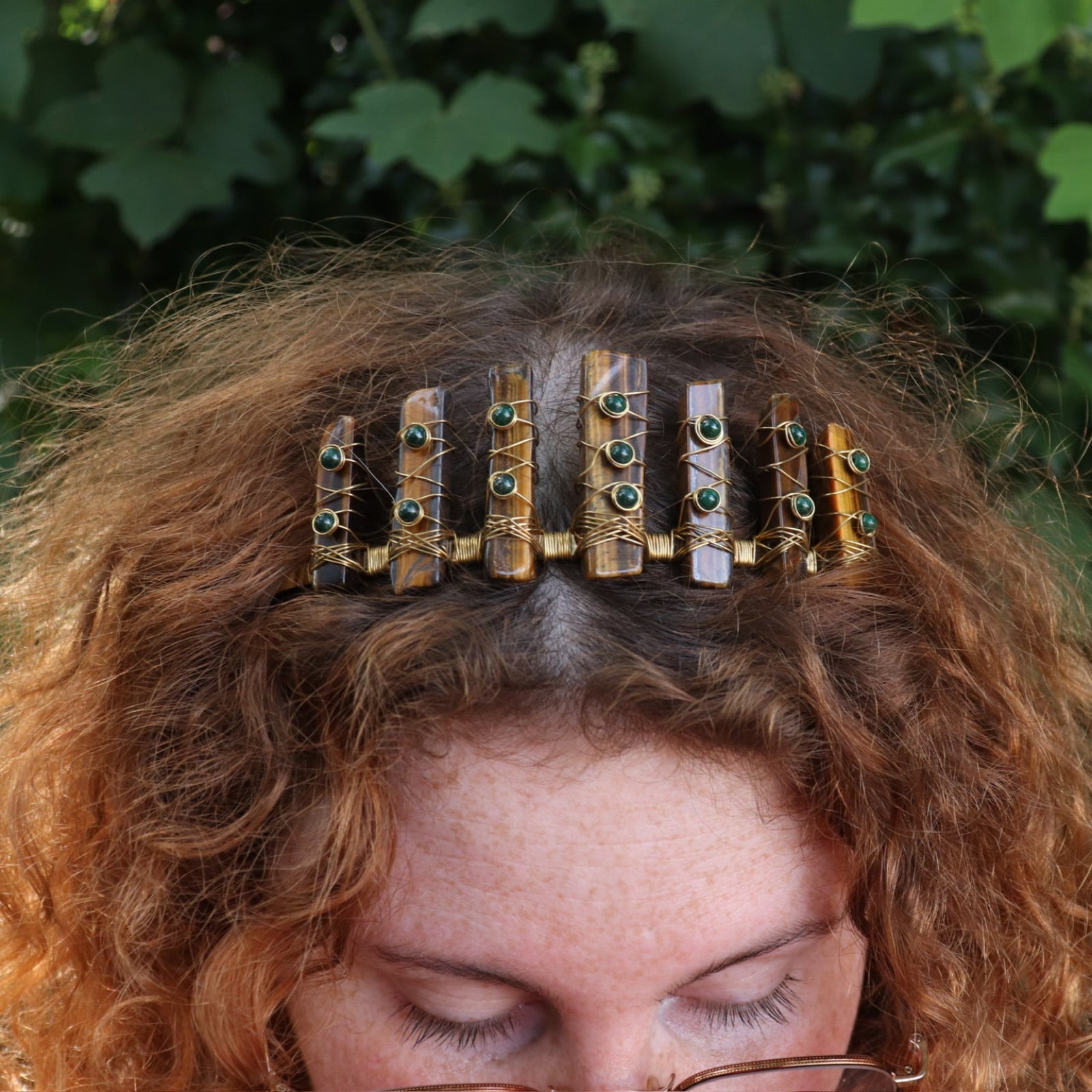 A woman wearing the Tigers Eye & Malachite Tiara in front of greenery.