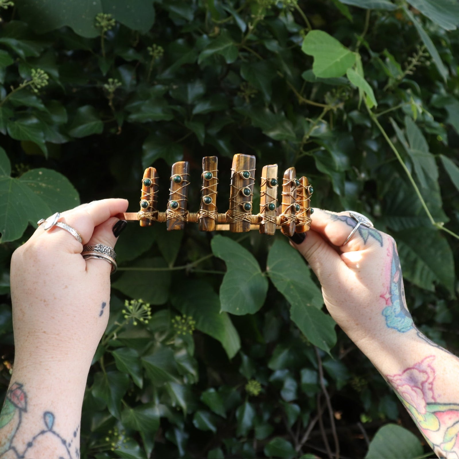 Someone holding the Tigers Eye & Malachite Tiara in front of greenery.