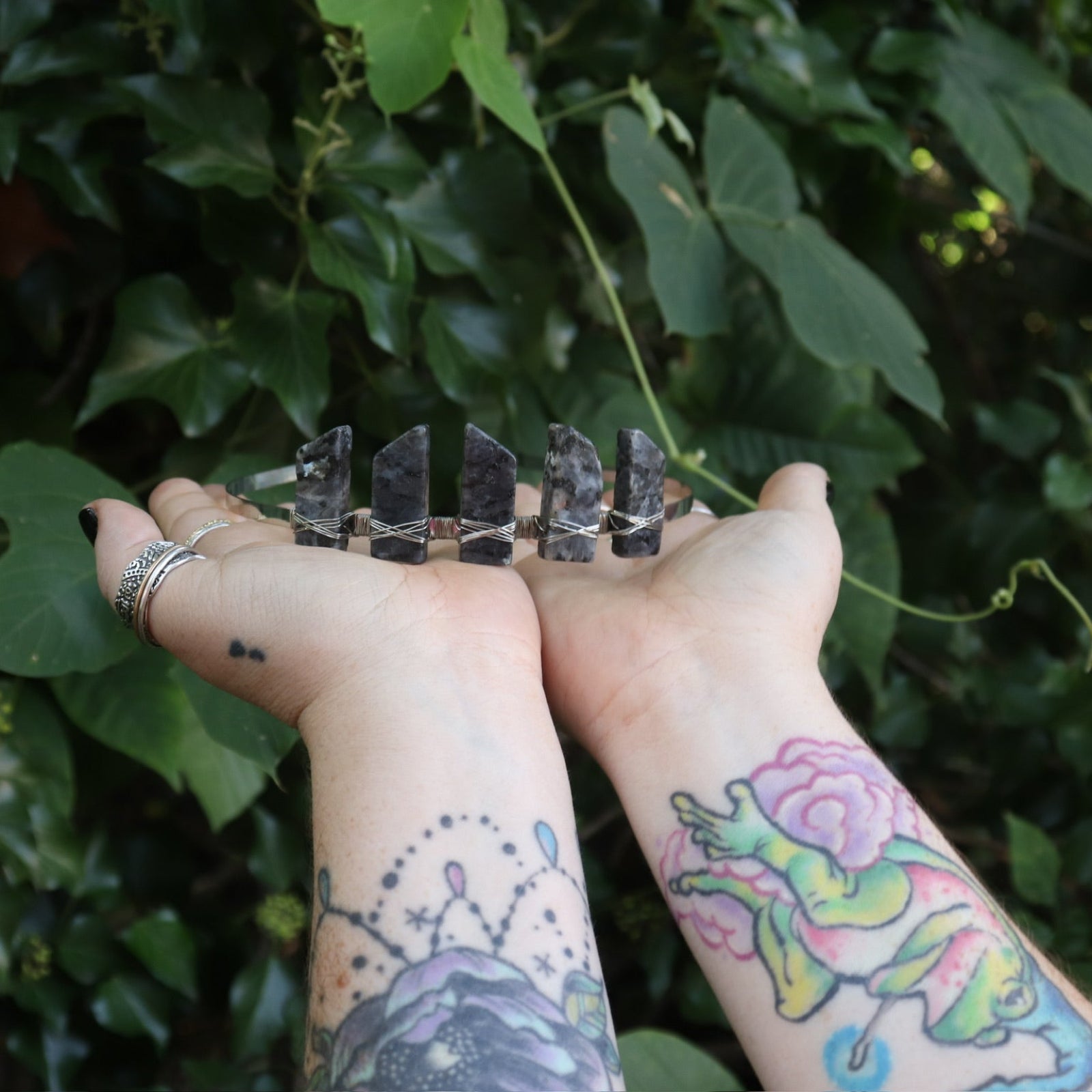 Someone holding the Fairy Crown / Celtic Tiara - Black Labradorite / Larvikite in front of greenery.