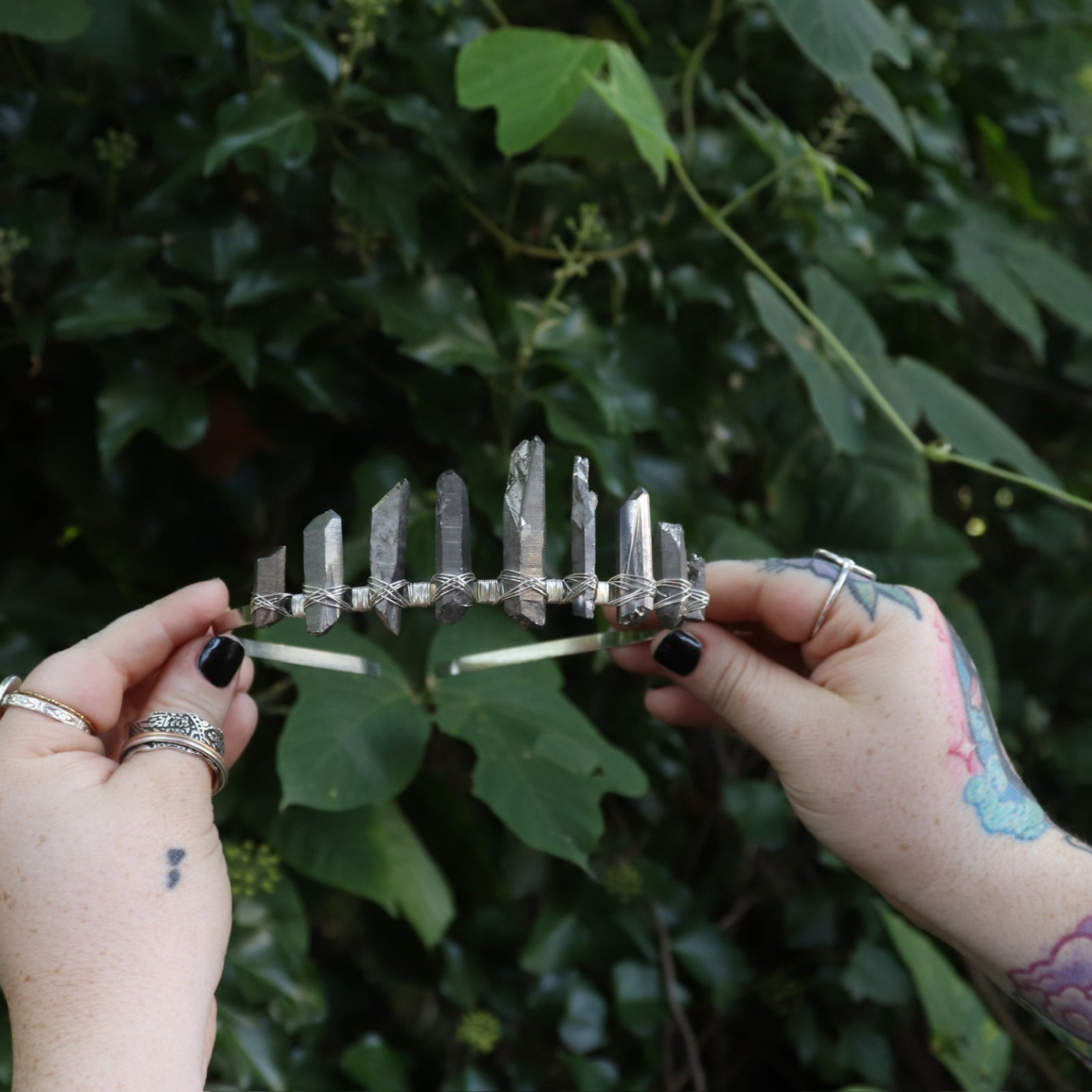 Someone holding the Fairy Crown / Celtic Tiara - Titanium Quartz in front of greenery.