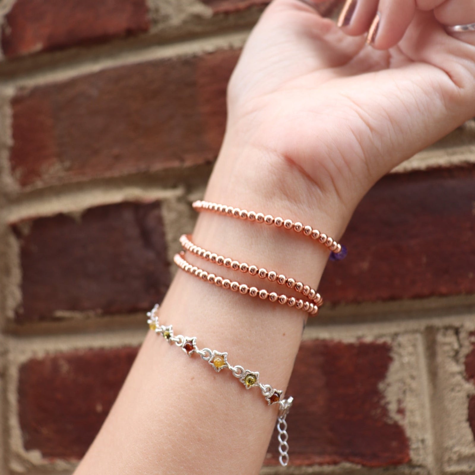 Someone wearing all the crystal faceted beads + Copper Bracelets in front of a brick wall.