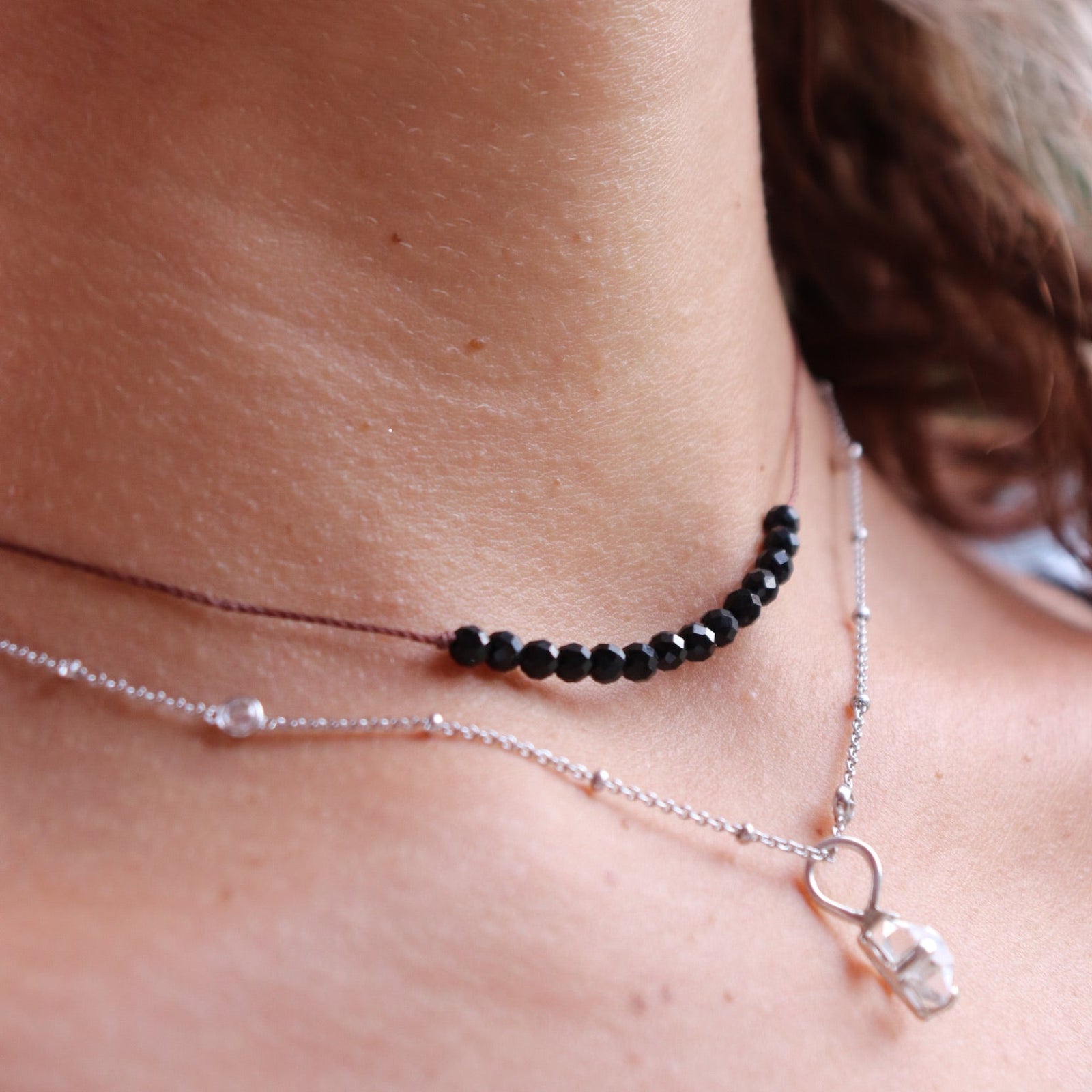 Someone wearing the Dainty 4mm Faceted Black Tourmaline Cord 16"-18" Necklace with another silver necklace.