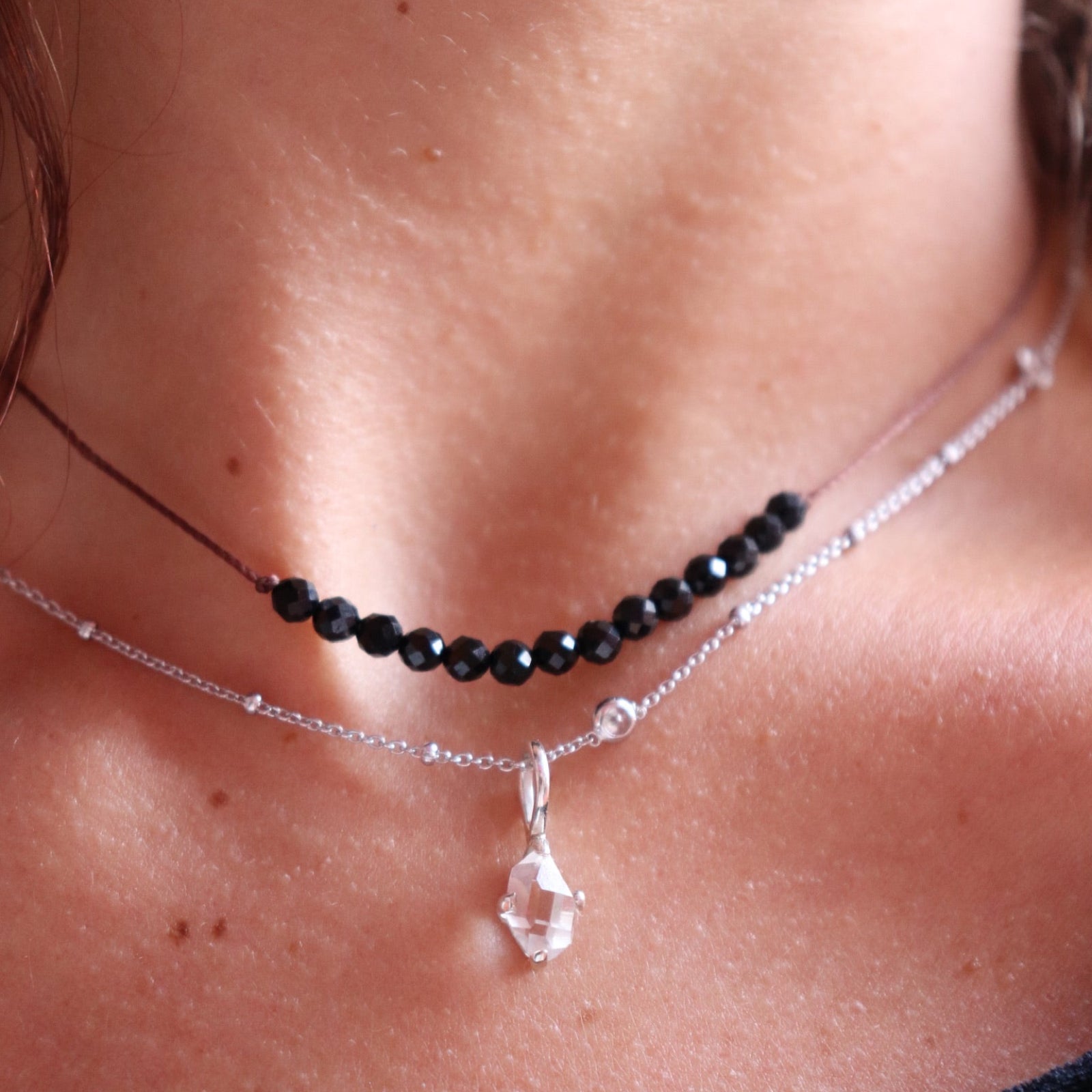 Someone wearing the Dainty 4mm Faceted Black Tourmaline Cord 16"-18" Necklace with another silver necklace.