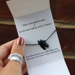 Someone holding the Black Tourmaline Healing Adjustable Band with an Affirmation in front of a brick wall.