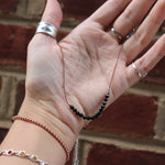 Someone holding the Dainty 4mm Faceted Black Tourmaline Cord 16"-18" Necklace in front of a brick wall.