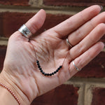 Someone holding the Dainty 4mm Faceted Black Tourmaline Cord 16"-18" Necklace in front of a brick wall.
