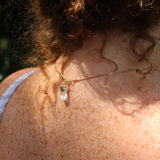 A woman wearing the Mini Rose Quartz Crystal Pendulum Necklace, showing off the back.
