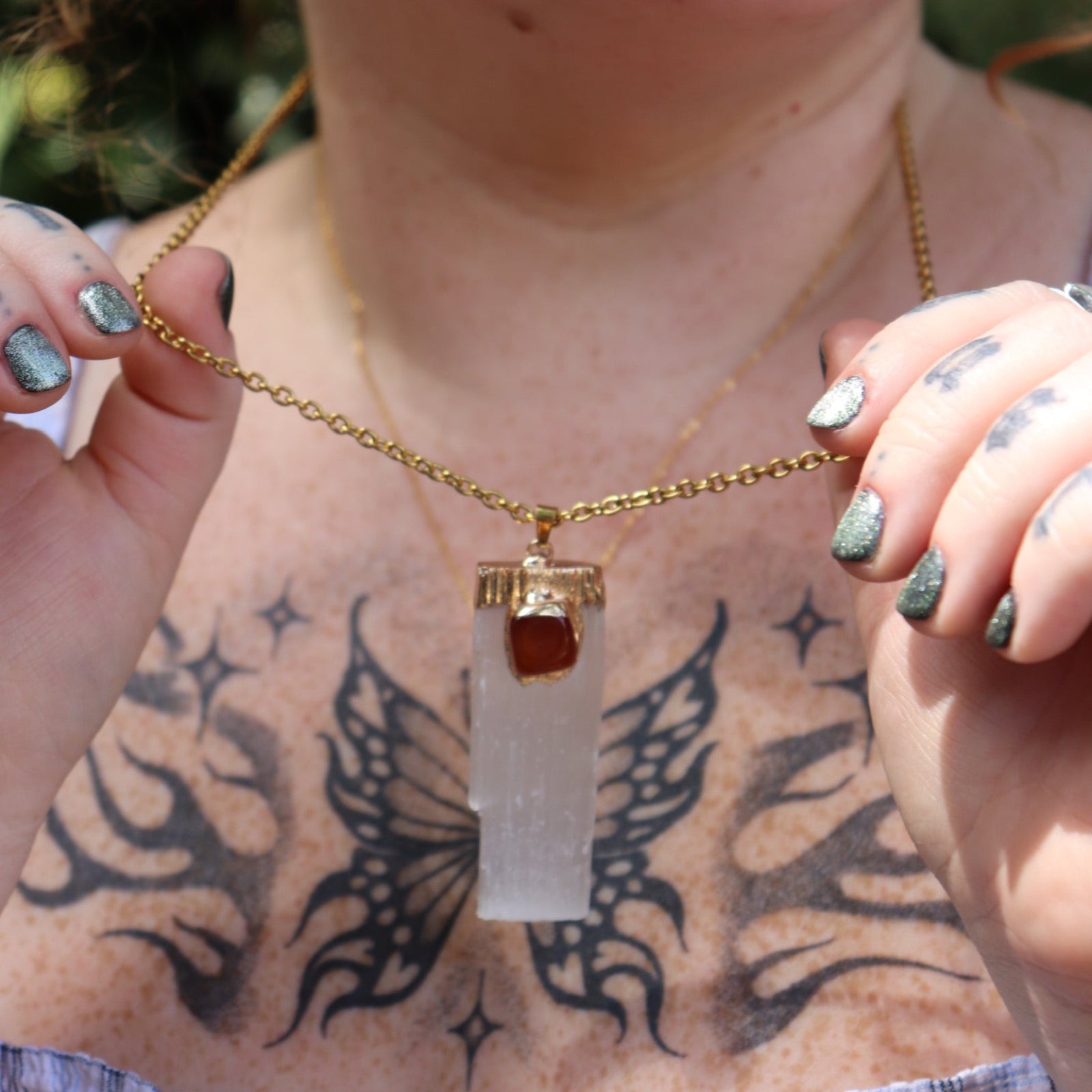 A woman wearing and holding the Selenite Carnelian Gold Adjustable Necklace with a blue top.