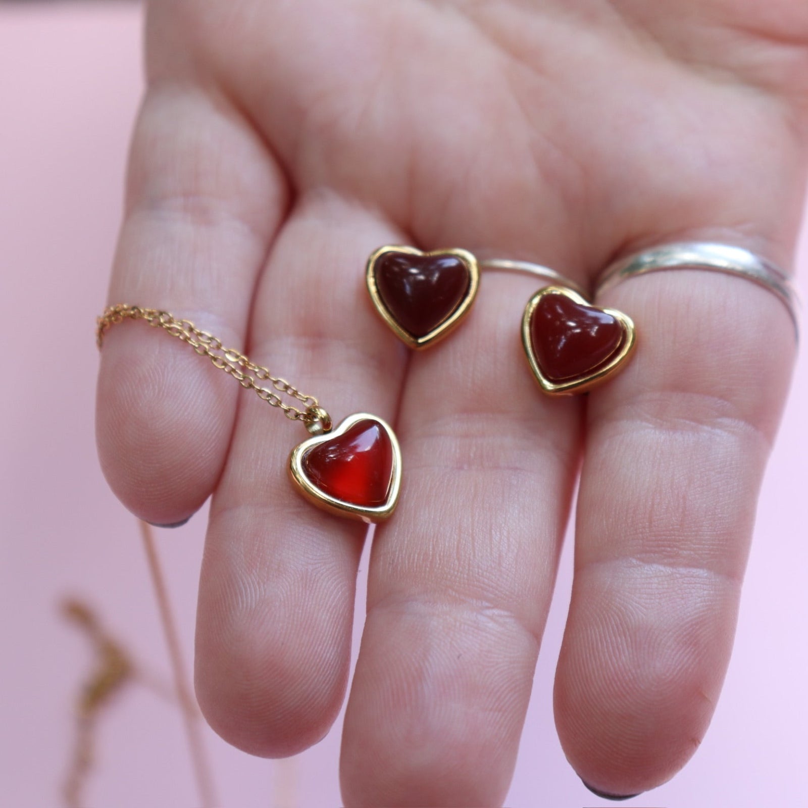 Someone holding the gold Carnelian Earrings & Necklace Gift Jewelry Set in front of a pink background.