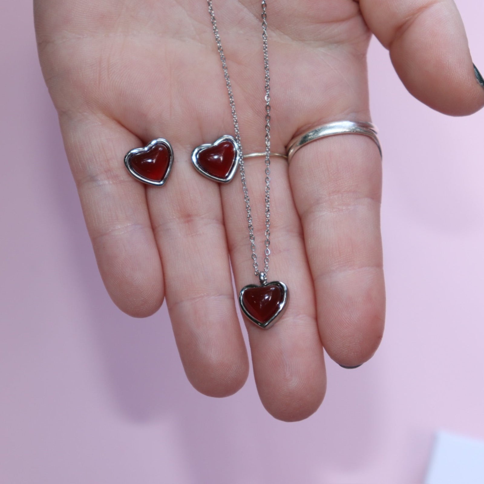 Someone holding the silver Carnelian Earrings & Necklace Gift Jewelry Set in front of a pink background.