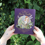 Someone holding the Book of Faerie Spells by Cheralyn Darcey in front of greenery.