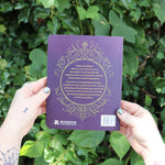 Someone holding the Book of Faerie Spells by Cheralyn Darcey in front of greenery, showing off the back.