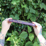 Someone holding the Book of Faerie Spells by Cheralyn Darcey in front of greenery, showing off the side.