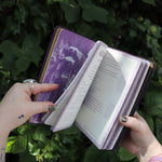 Someone holding the Book of Faerie Spells by Cheralyn Darcey open in front of greenery, showing off the pages.