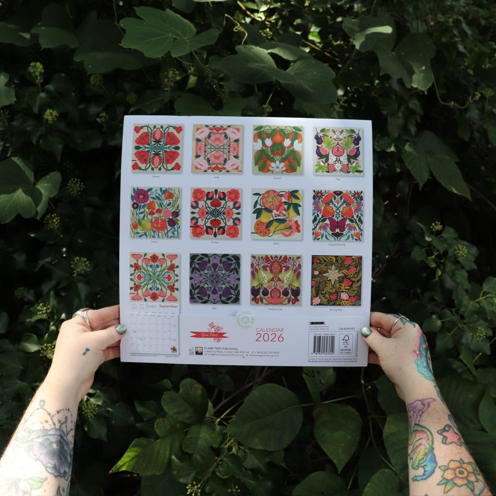 Someone holding the Nina Pace Wall Calendar 2026 in front of greenery, showing off the back.