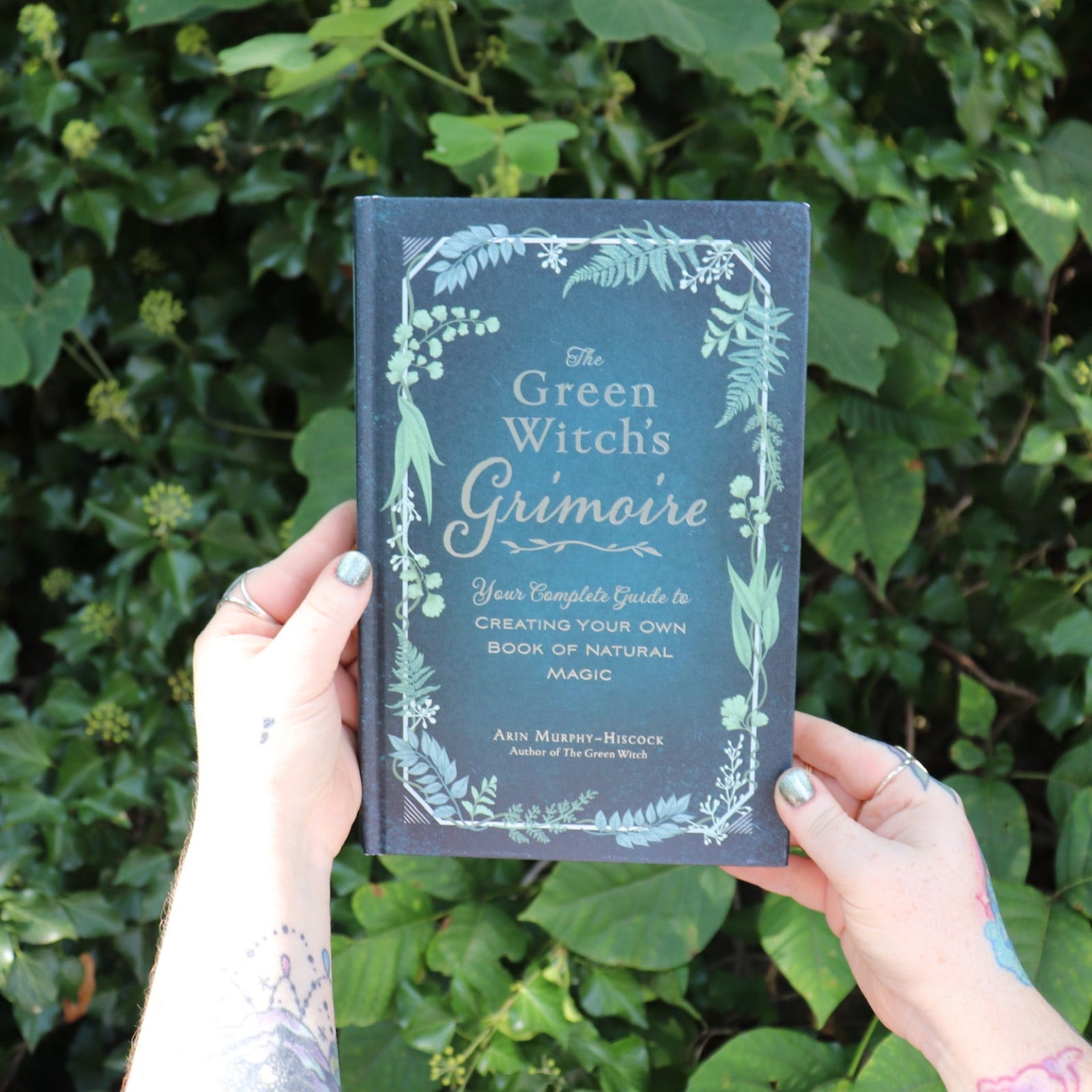 Someone holding the Green Witch's Grimoire by Arin Murphy-Hiscock in front of greenery.