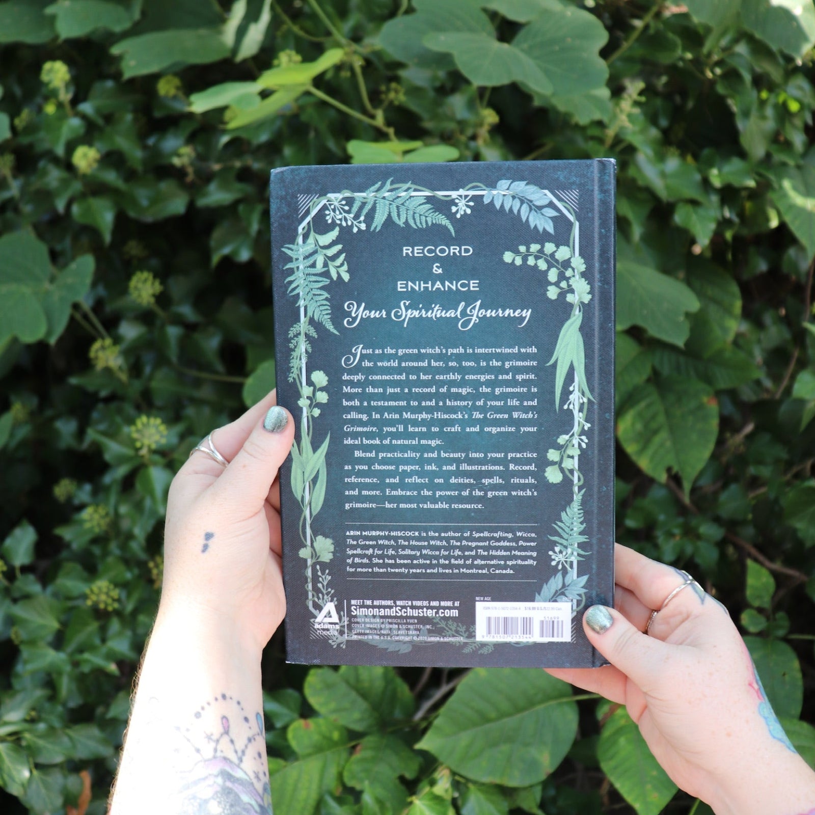 Someone holding the Green Witch's Grimoire by Arin Murphy-Hiscock in front of greenery, showing off the back.