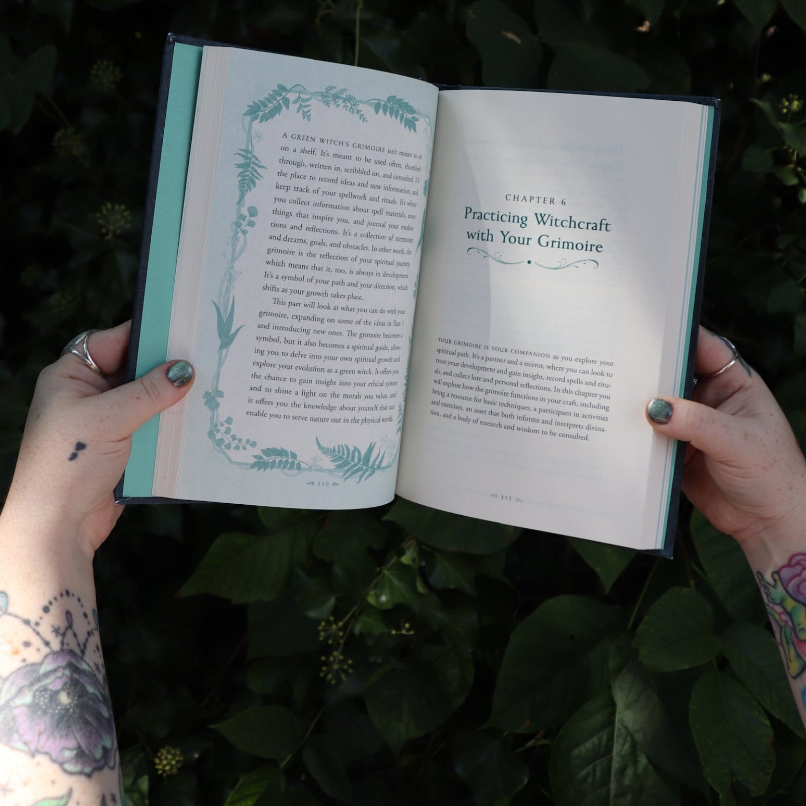 Someone holding the Green Witch's Grimoire by Arin Murphy-Hiscock open in front of greenery, showing off the pages.