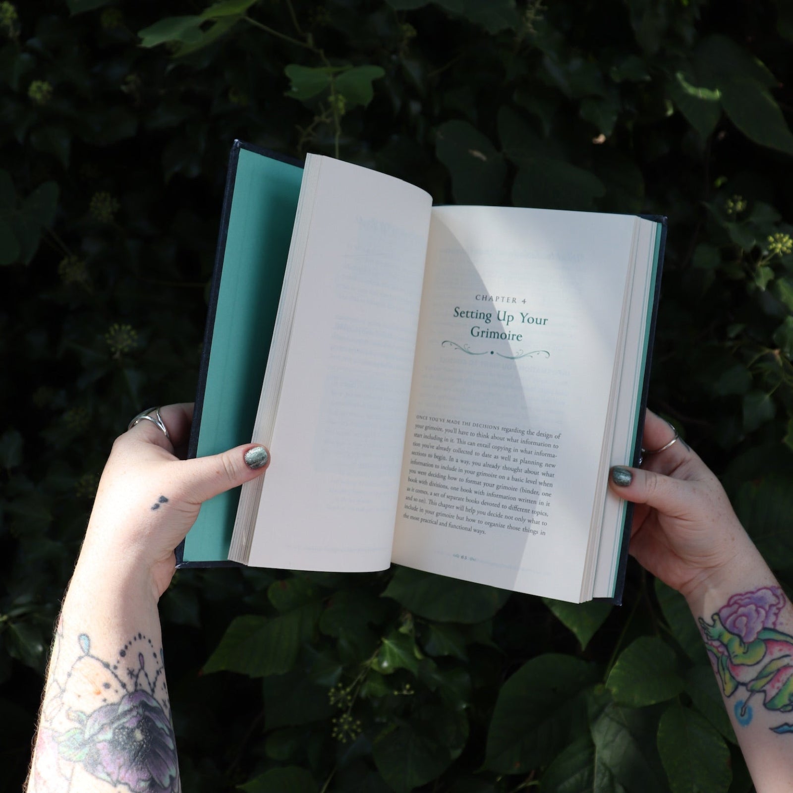 Someone holding the Green Witch's Grimoire by Arin Murphy-Hiscock open in front of greenery, showing off the pages.