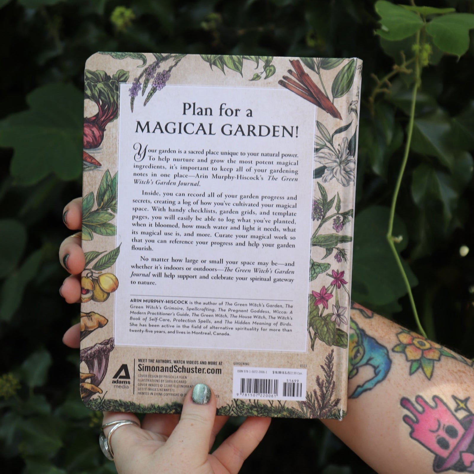 Someone holding the Green Witch's Garden Journal by Arin Murphy-Hiscock in front of greenery, showing off the back.