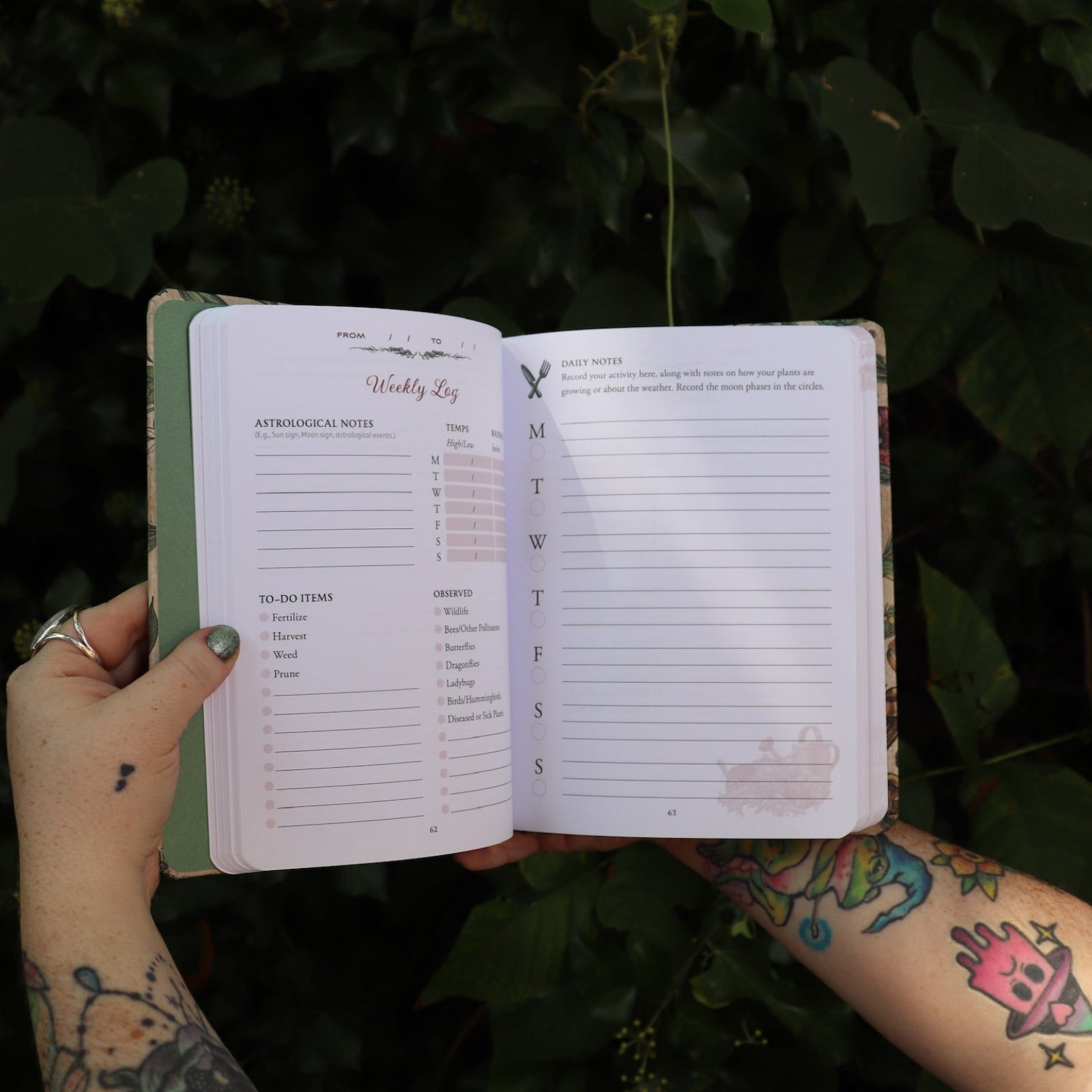 Someone holding the Green Witch's Garden Journal by Arin Murphy-Hiscock open in front of greenery, showing off the pages.