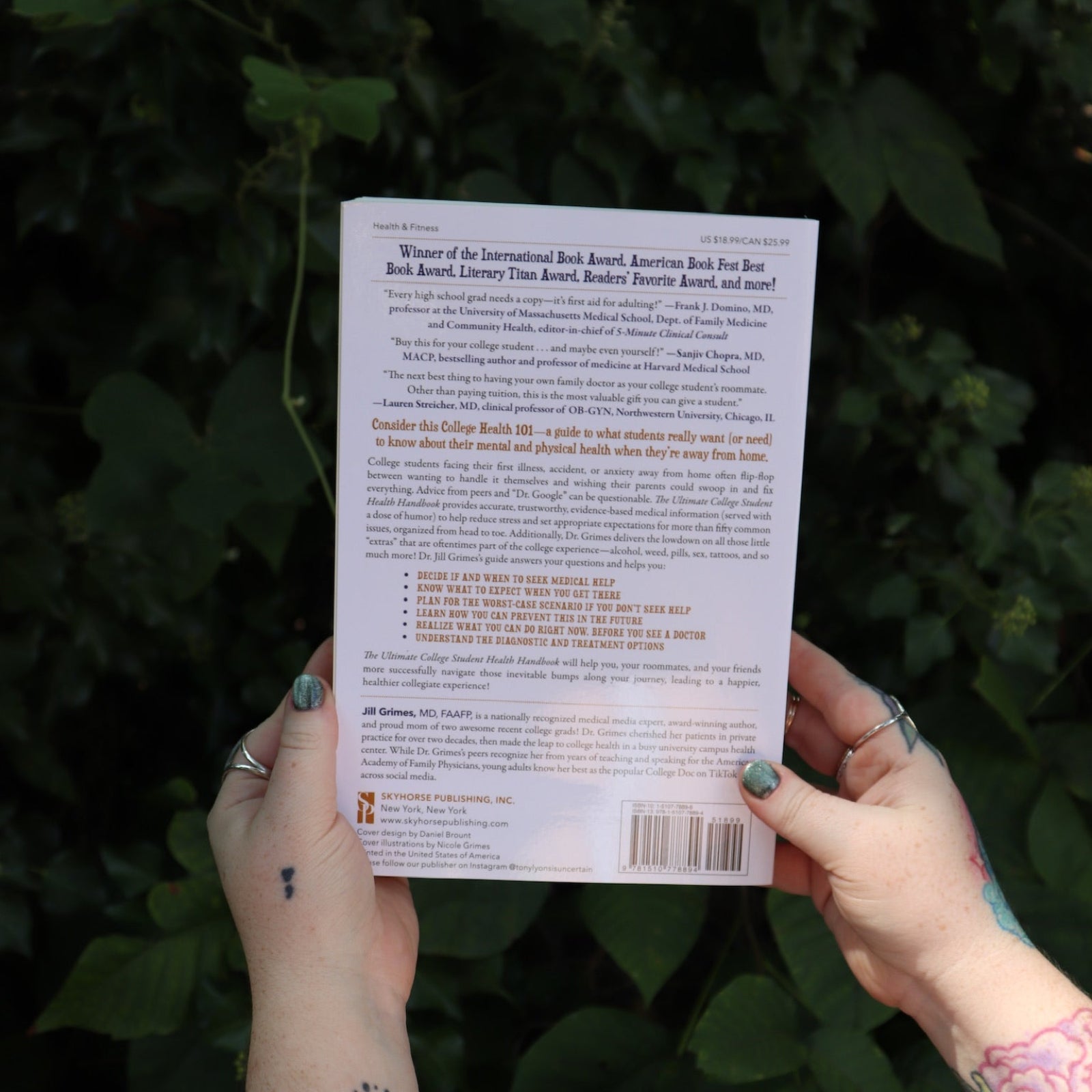 Someone holding the Ultimate College Student Health Handbook by Jill Grimes in front of greenery, showing off the back.