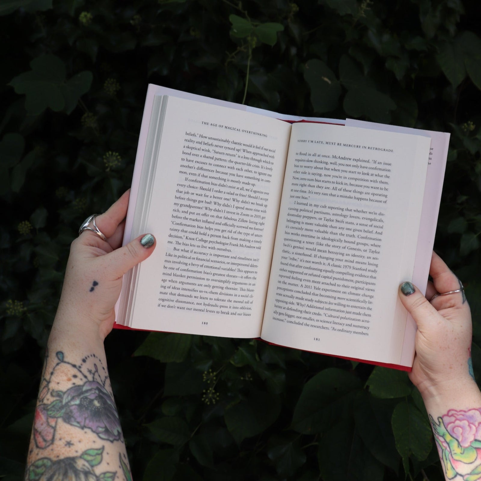 Someone holding the Age of Magical Overthinking Hardcover Book open in front of greenery, showing off the pages.