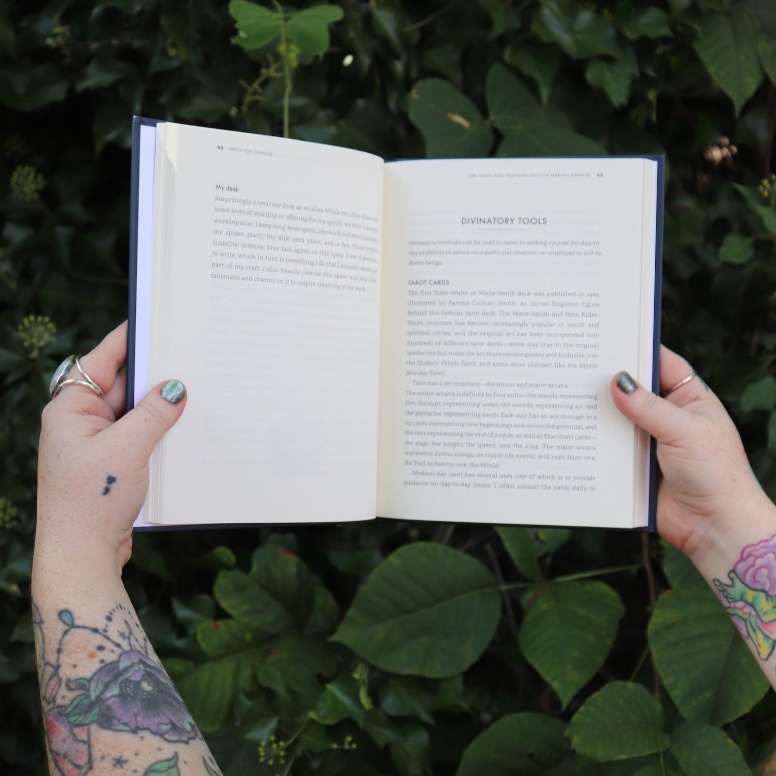 Someone holding the Spells for Change Hardcover Book open in front of greenery, showing off the pages.