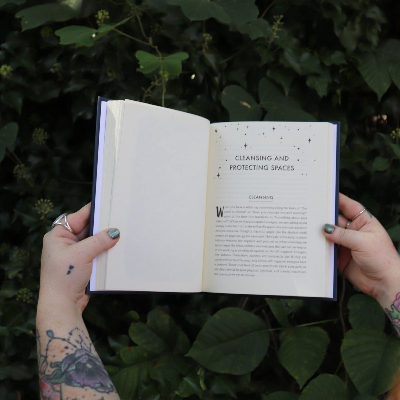 Someone holding the Spells for Change Hardcover Book open in front of greenery, showing off the pages.