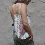 A woman wearing blue pants and a halter top with the African Off White and Tan Mud Cloth Tote with Pink Faux Fur on her shoulder all in front of a white wall.