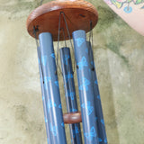An up close image of someone holding the Butterfly Woodstock Garden Chime™ in front of a concrete wall.