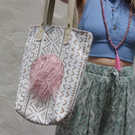 A woman wearing blue pants and a halter top with the African Off White and Tan Mud Cloth Tote with Pink Faux Fur on her shoulder all in front of a white wall.