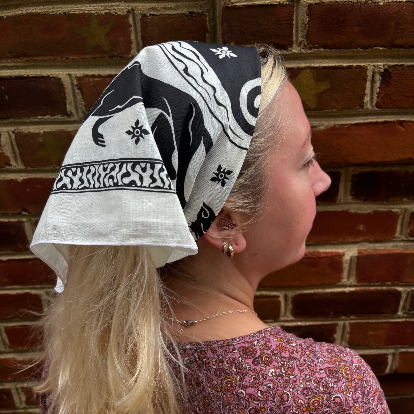 A woman wearing the Screenprinted Chat Noir Cotton Bandana around her head.