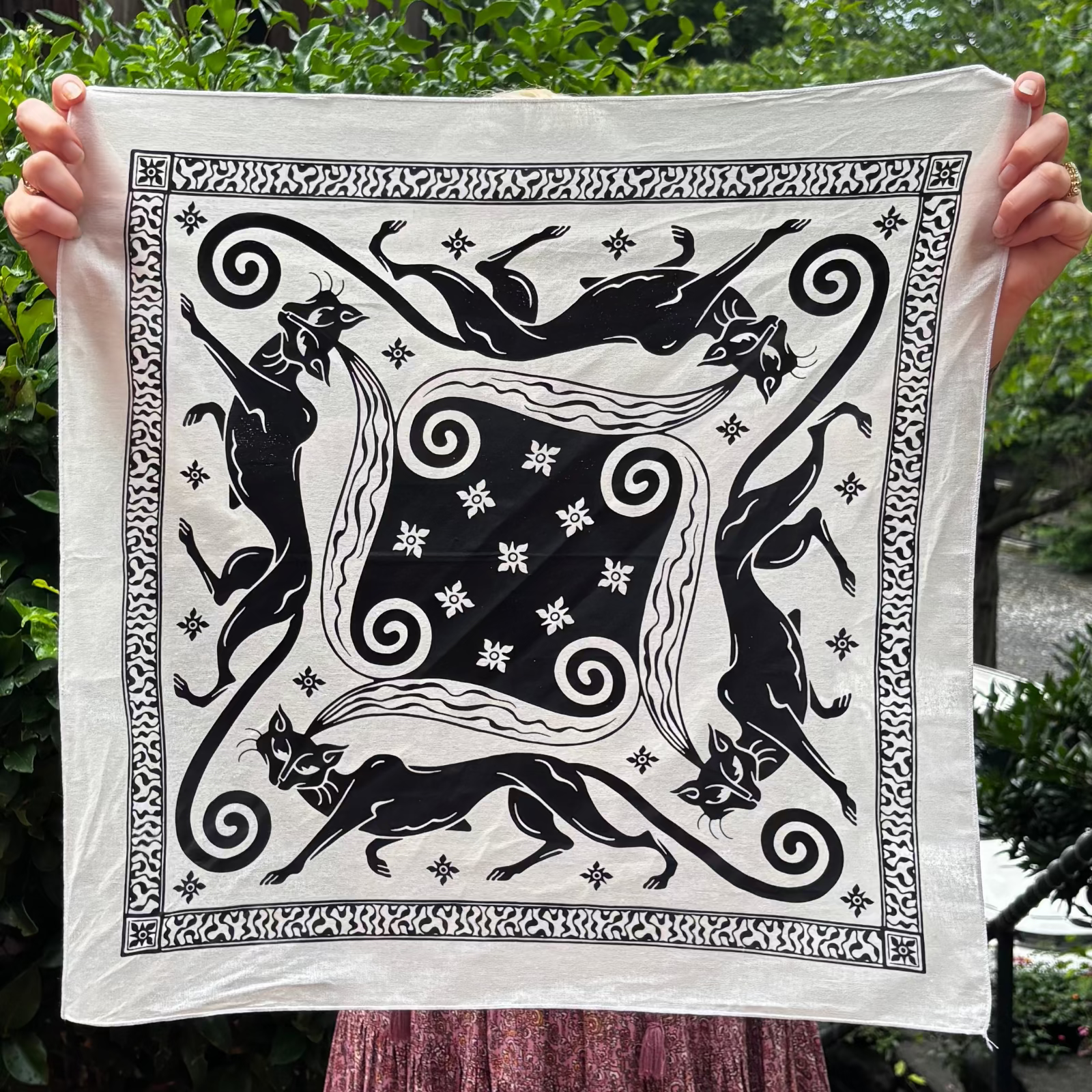 Someone holding the Screenprinted Chat Noir Cotton Bandana up to show off its design.