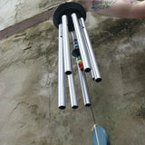 An up-close image of someone holding up the Seven Stone Blue Woodstock Chakra Chime in front of a concrete wall.