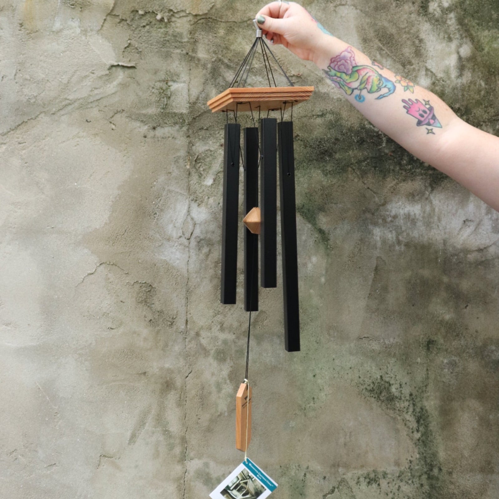 Someone holding the Black Woodstock Craftsman Chime in front of a concrete wall.