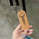 An up-close image of someone holding the Black Woodstock Craftsman Chime in front of a concrete wall.