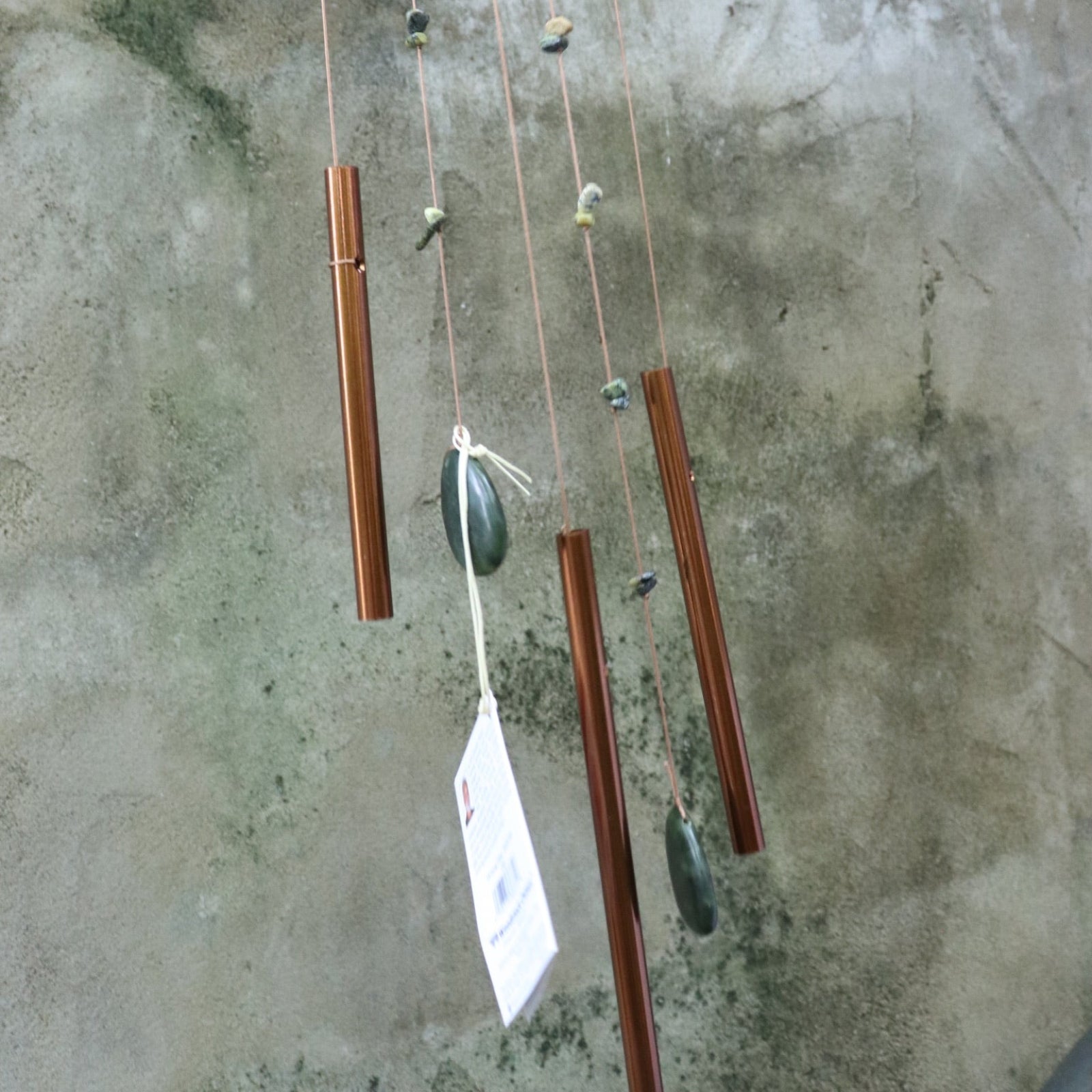 Someone holding the Small Jade Chi Energy Wind Chime in front of a concrete wall.