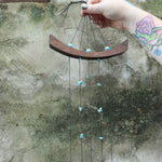 An up-close image of someone holding the Small Turquoise Chi Energy Wind Chime in front of a cement wall.