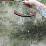 An up-close image of someone holding the Small Turquoise Chi Energy Wind Chime in front of a cement wall.