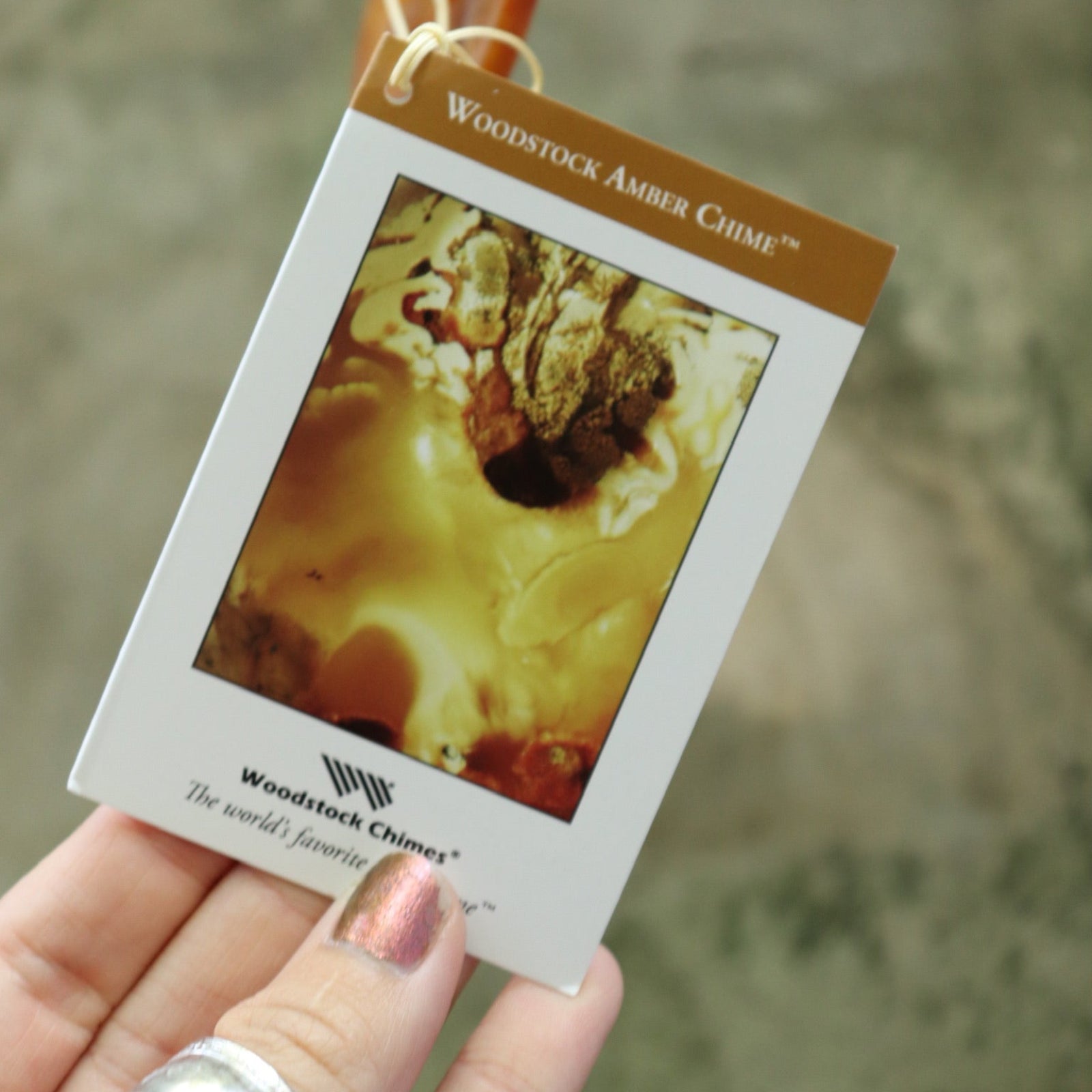 An up-close image of someone holding the tag of the Woodstock Amber Wind Chime.