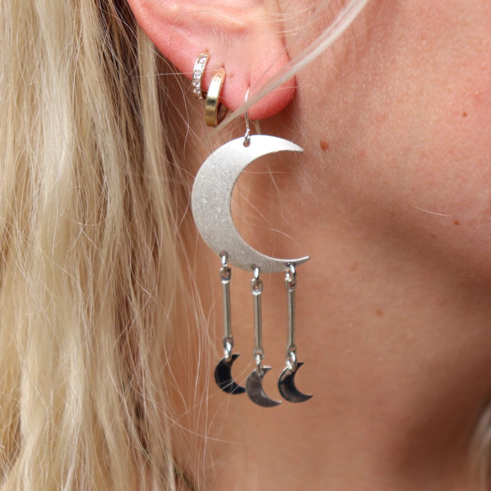 A woman wearing the Silver Many Moons 2.5 inch. Earrings.