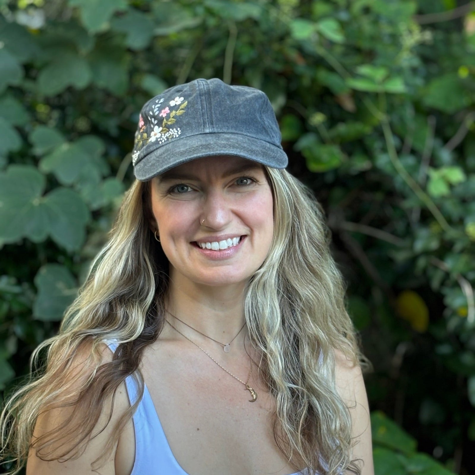 A woman wearing the Flower Garden Embroidered Adjustable Baseball Cap in front of greenery.