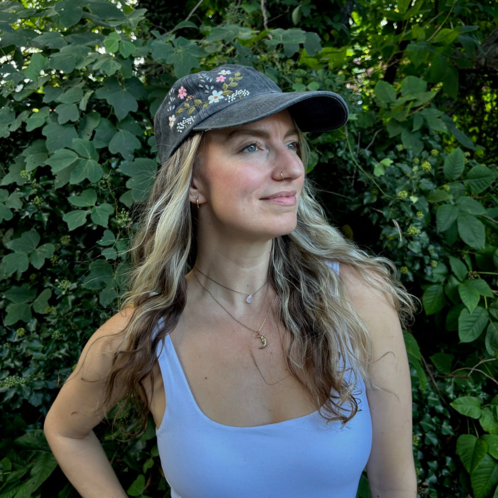 A woman wearing the Flower Garden Embroidered Adjustable Baseball Cap in front of greenery.