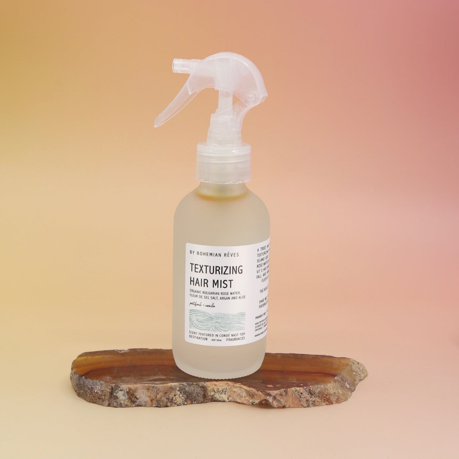 The Patchouli Vanilla Sea Salt Texturizing Hair Mist by Bohemian Rêves on an agate slice all on a pink and yellow background