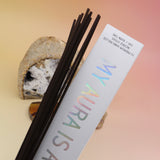 The My Aura Is A Prism Hand-Rolled Incense Sticks Package in front of an agate slice, open geode, and a selenite tower all on a pink and yellow background.