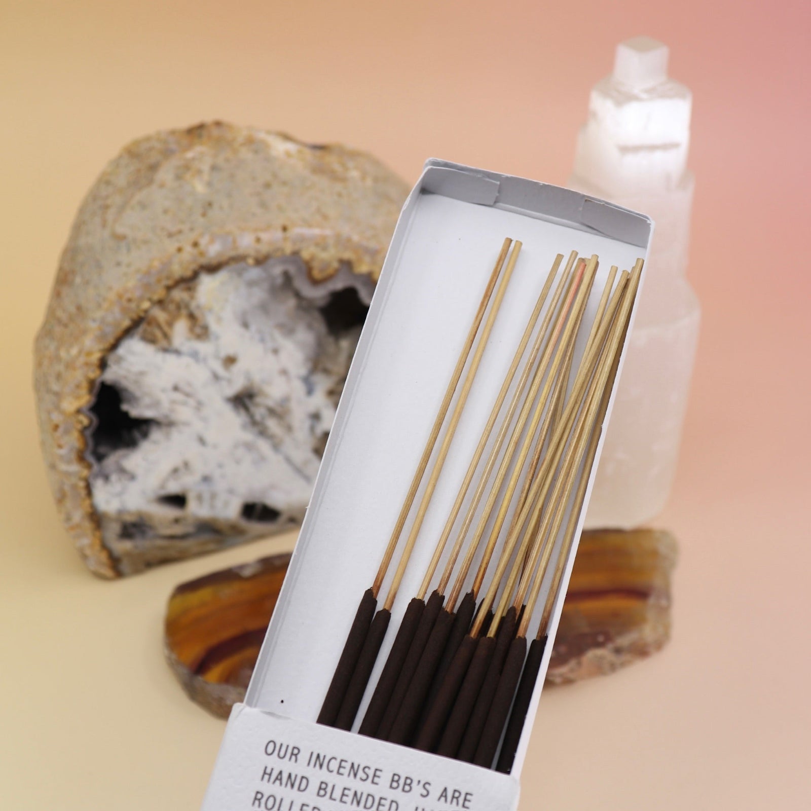 A Bohemian Reves open package in front of an agate slice, open geode, and a selenite tower all on a pink and yellow background.