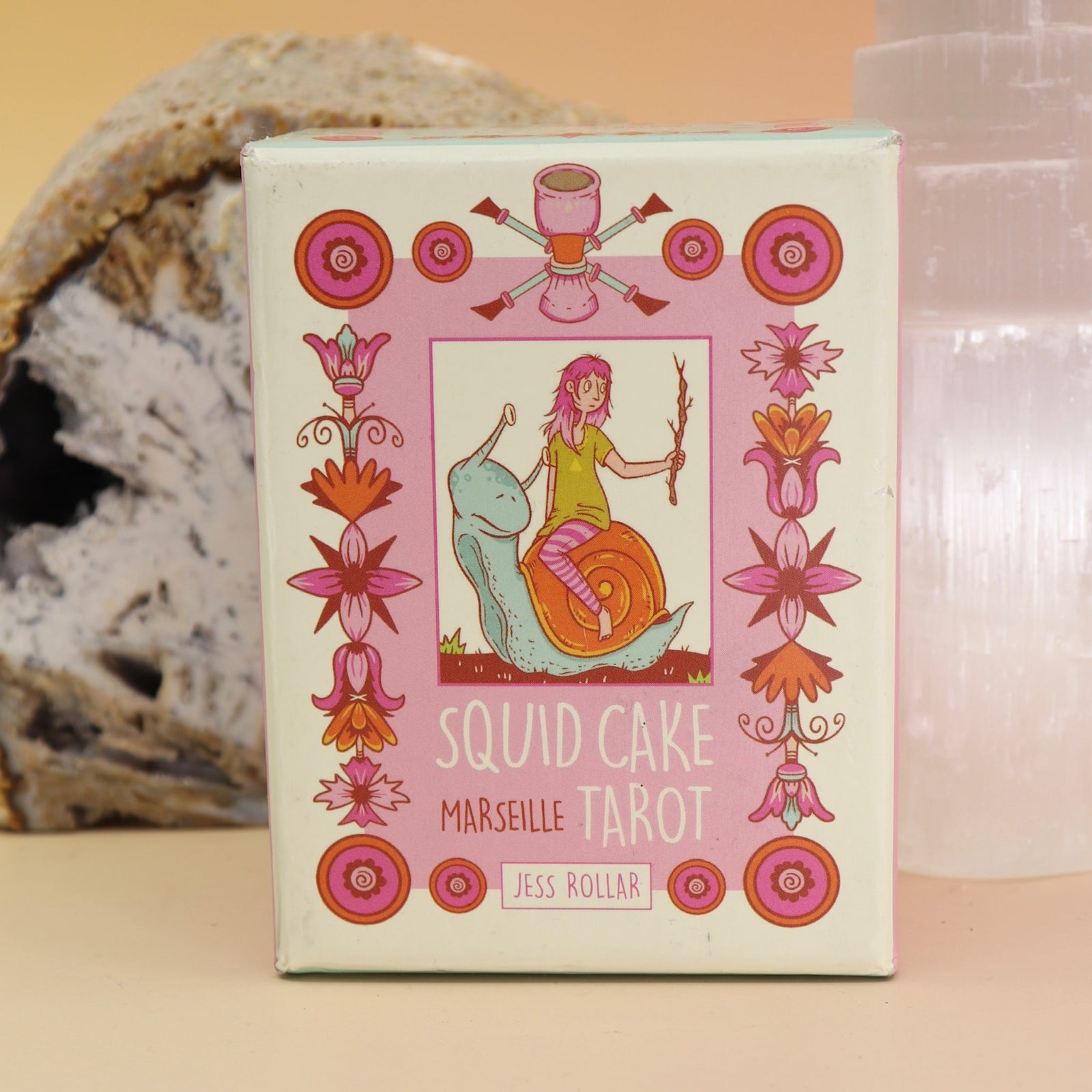 The Squid Cake Marseille Tarot Deck in front of a selenite tower and an agate slice all on a pink and yellow background.