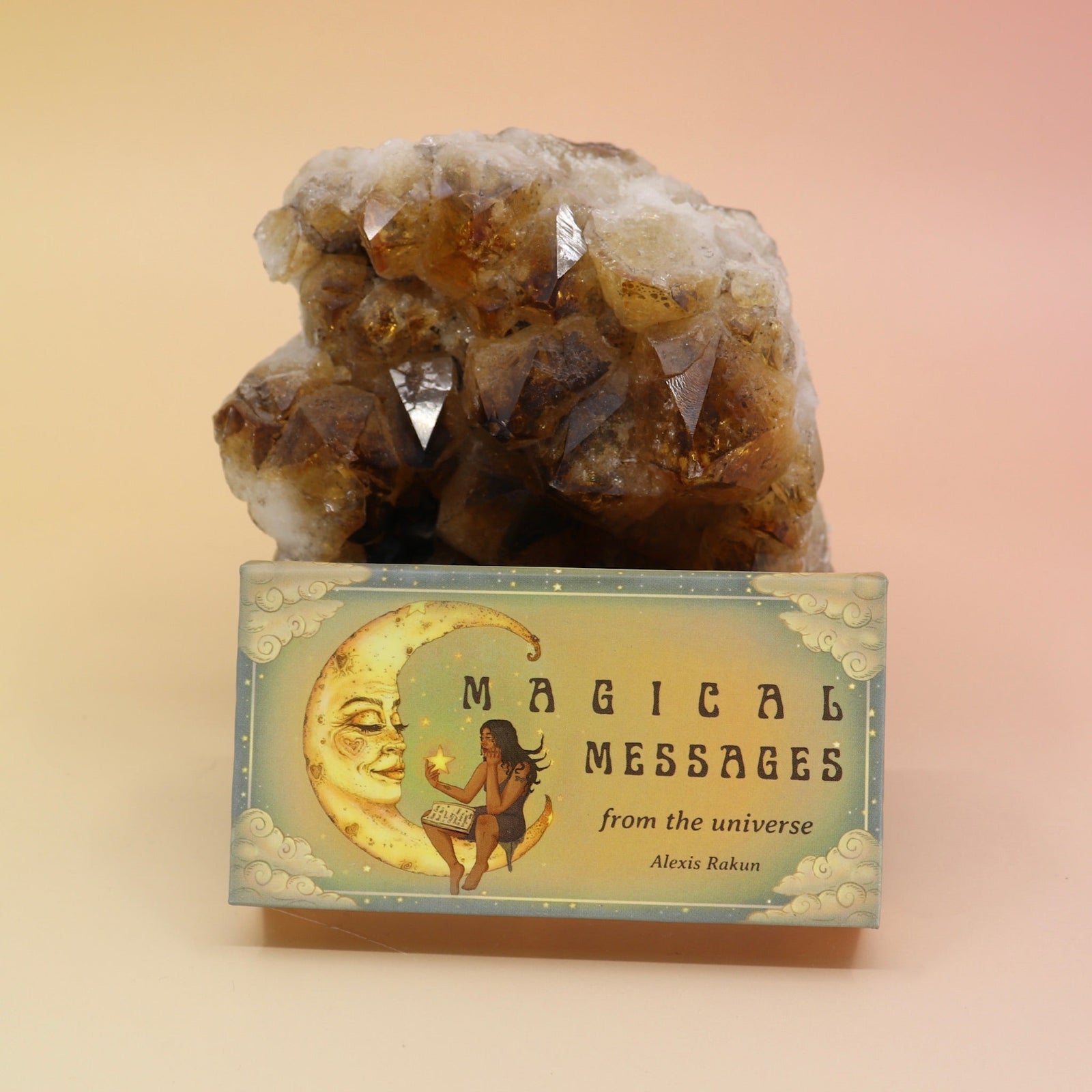 The Magical Messages from the Universe Affirmation + Divination Cards leaning against a citrine piece all on a pink and yellow background.